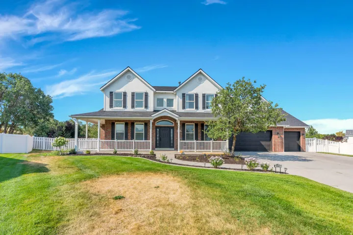 Two-story residence featuring a covered front porch with white railings, brick and siding exterior, multiple gables, and a two-car garage with a paved driveway