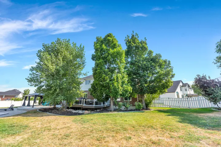 Expansive backyard featuring a large lawn, mature trees, and an elevated deck with white railings