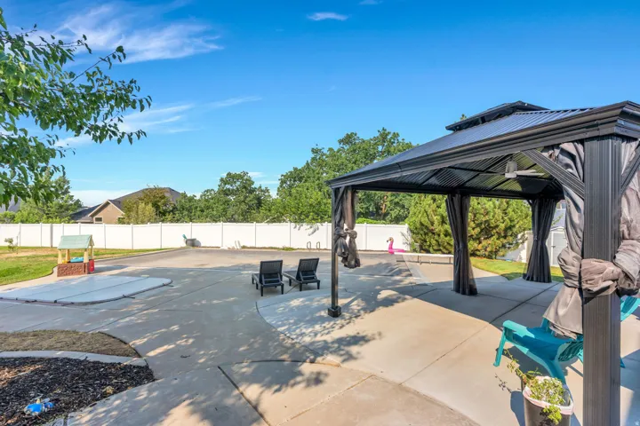 Expansive concrete patio with a covered gazebo, defined landscape beds, and a white privacy fence
