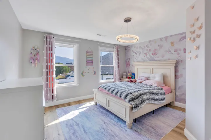 Wood-finish flooring, dual windows, decorative wall accents, and an overhead chandelier with a crystal-like design
