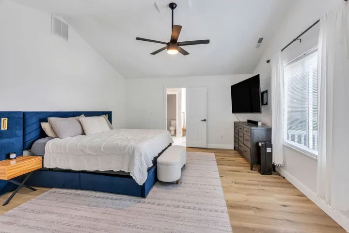 Vaulted ceiling with a ceiling fan, white walls, wood-finish flooring, and a white framed window