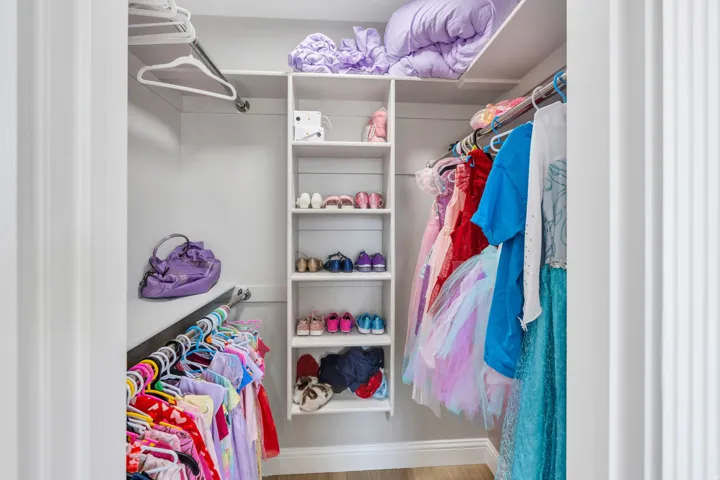 Custom closet organization system featuring a central shelving unit, multiple hanging rods, and an upper storage shelf