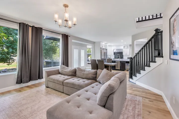 Open-concept living space featuring wood-finish flooring, a modern chandelier, and a black staircase with white risers