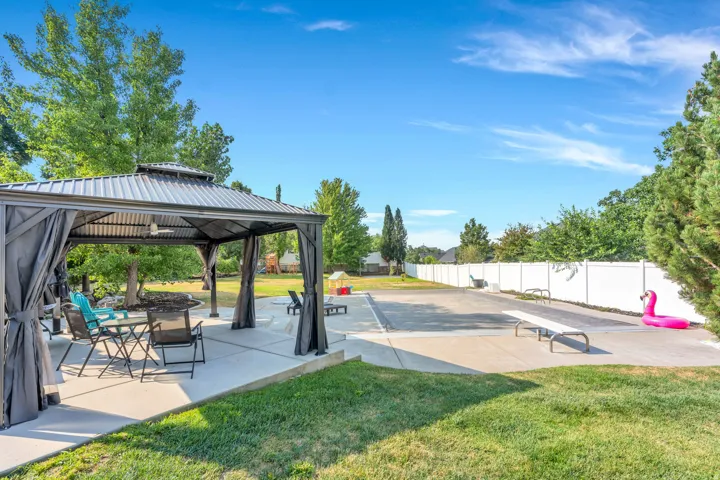 Expansive outdoor space featuring a covered gazebo, paved patio, and a fenced yard with mature trees