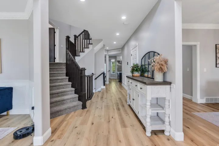 Light wood-finish flooring extending through the entry, crown molding details, wainscoting, a staircase with dark wood newel posts and handrails, and recessed lighting