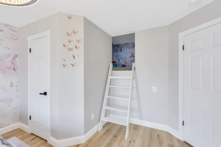 Wood-finish flooring, white paneled doors with black hardware, and a built-in ladder feature