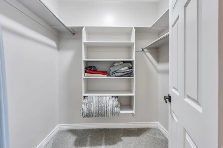 Built-in shelving, hanging rods, light gray wall paint, white trim, and gray carpet
