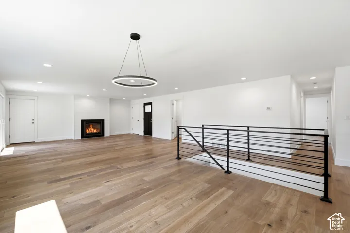 Hardwood-style flooring throughout, modern recessed lighting, white brick fireplace, contemporary ring chandelier, and sleek black metal railing