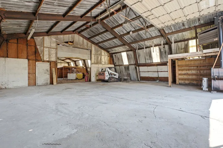 Exposed metal beam ceiling, concrete flooring, overhead roll-up door, interior wood paneling, and an interior wood-frame structure