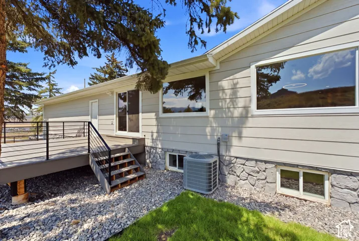 Exterior siding, stone foundation, multi-level deck with metal railings, sliding glass door, and large windows
