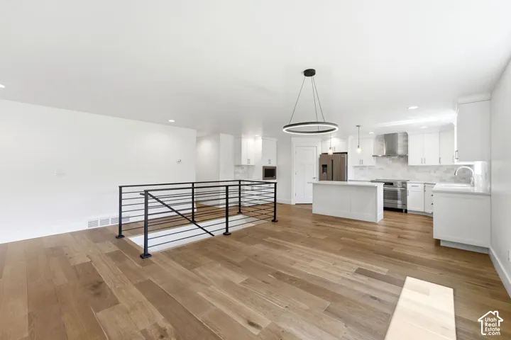 Wide-plank wood-finish flooring, white walls, black metal railing, white shaker cabinetry, and stainless steel appliances