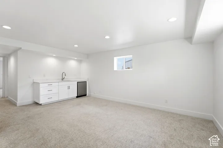 Recessed lighting throughout, built-in wet bar with white cabinetry, stainless steel sink with gooseneck faucet, integrated beverage refrigerator, and a window providing natural light