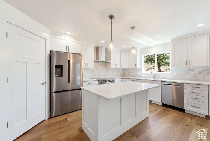 Modern kitchen featuring white cabinetry, stainless steel appliances, wood-finish flooring, a center island with a light-toned countertop, and a tiled backsplash