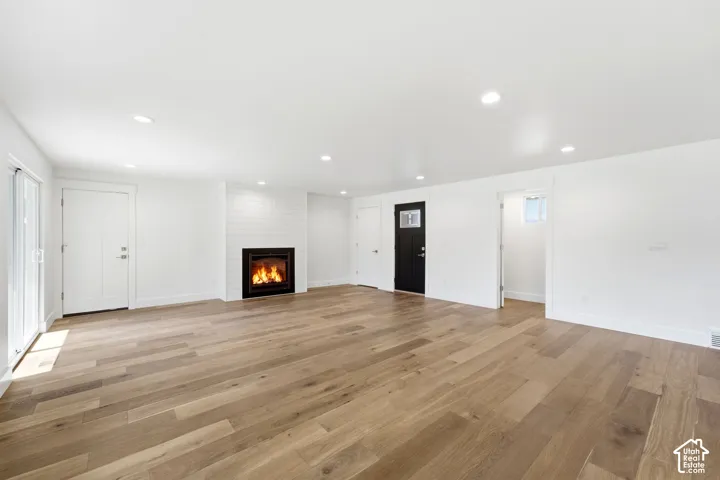 Spacious room featuring wood-finish flooring, a contemporary fireplace with white shiplap surround, recessed lighting, a sliding glass door, and a black paneled door