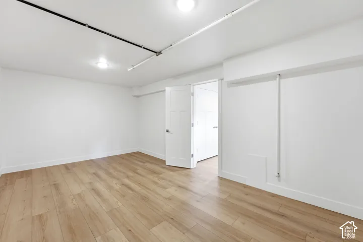 Light wood-finish flooring, white walls, recessed lighting, and a solid core interior door