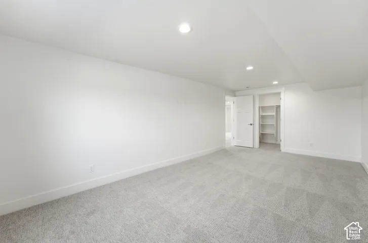 Spacious room featuring light gray carpeting, crisp white walls, recessed ceiling lighting, and a closet with built-in shelving