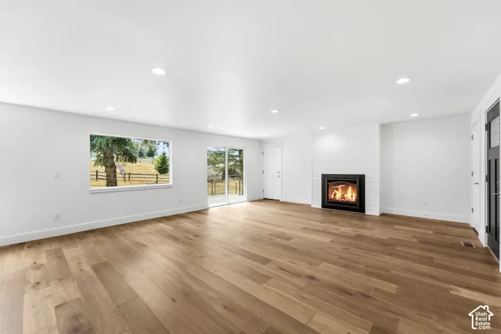 Expansive interior featuring wood-finish flooring, recessed lighting, a fireplace with shiplap surround, and large windows