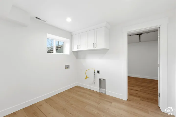 Recessed lighting, wood-finish flooring, white cabinetry, and a casement window