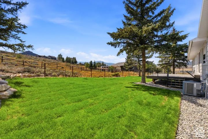 Expansive backyard featuring a manicured lawn, a wooden deck with black railings, and a wooden fence