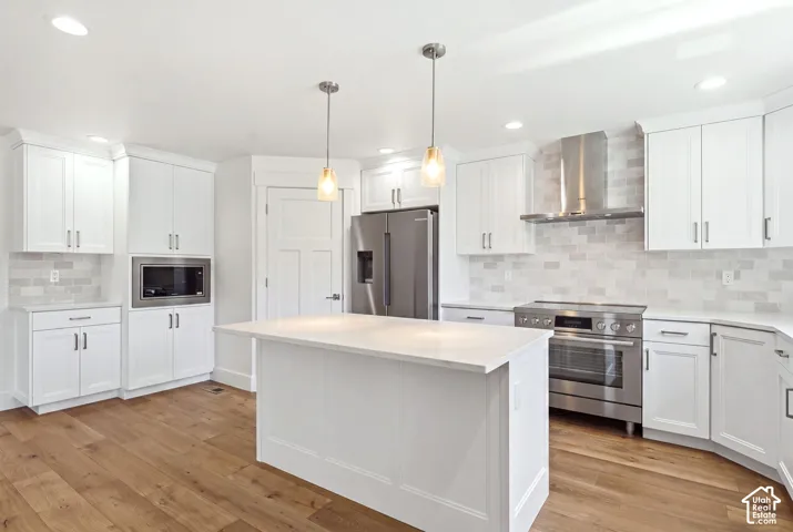 White shaker cabinetry, wood-finish flooring, central island with solid surface countertop, stainless steel appliances, and subway tile backsplash