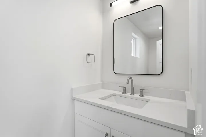 White vanity with shaker-style cabinetry, an undermount sink, and a stone countertop