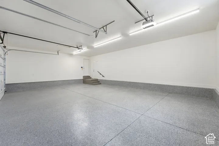 Spacious garage with an epoxy floor finish, overhead lighting, and an integrated staircase