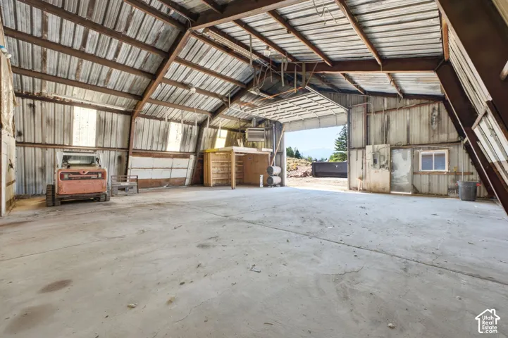 Metal-clad structure with a high-pitched roof and exposed beams, featuring a large overhead door and a concrete floor