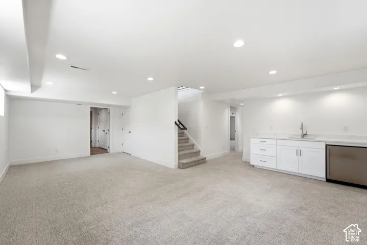 Spacious room featuring light-toned carpeting, recessed lighting, and a built-in wet bar with white cabinetry and a stainless steel appliance