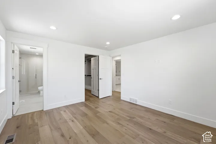 Wood-finish flooring, recessed lighting, white walls, built-in closet organization, and glass-enclosed shower
