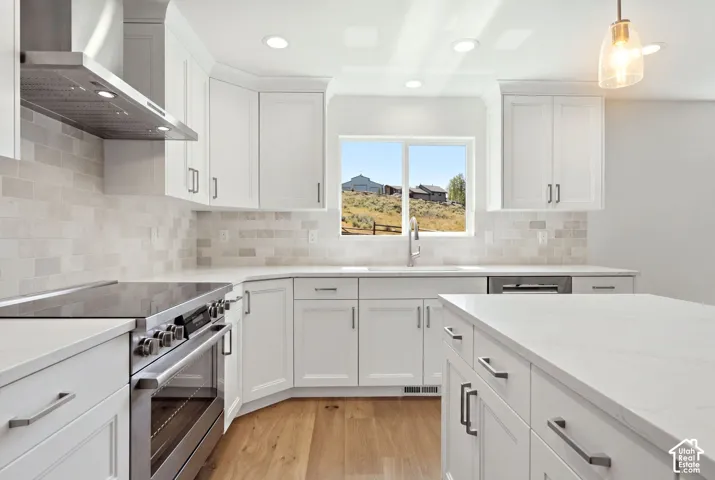 White cabinetry with brushed nickel hardware, stainless steel range and hood, light-toned backsplash, light-toned countertops, and wood-finish flooring