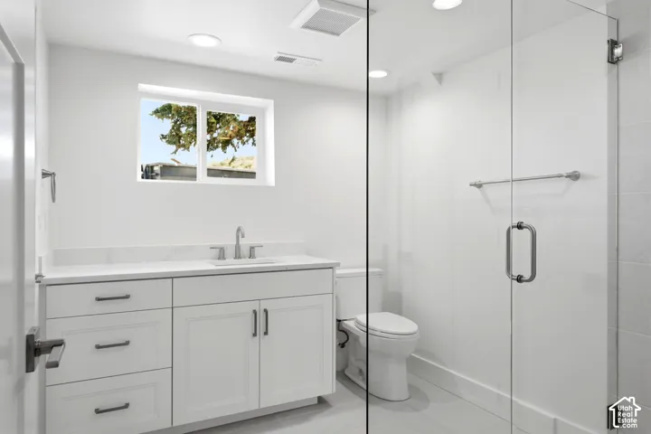 Modern bathroom featuring a white vanity with integrated sink, a frameless glass shower enclosure, recessed lighting, and a window for natural illumination