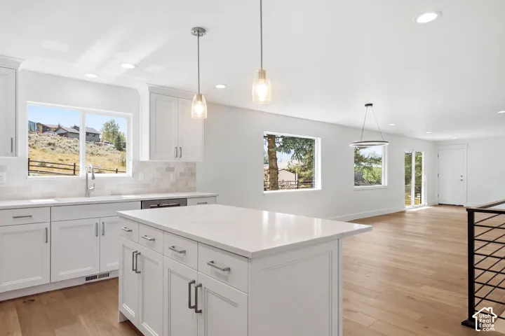 Contemporary kitchen featuring white cabinetry, a large center island with a stone countertop, a tile backsplash, and wood-finish flooring
