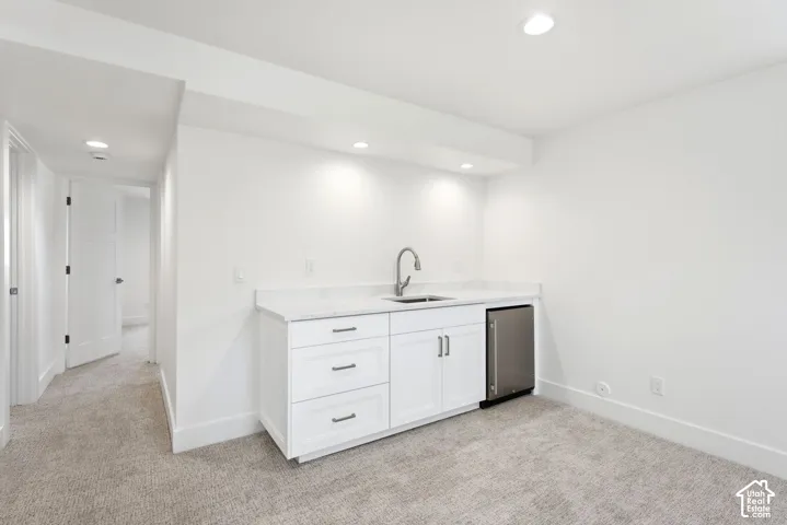 Wet bar with white cabinetry, stainless steel sink, and compact stainless steel refrigerator