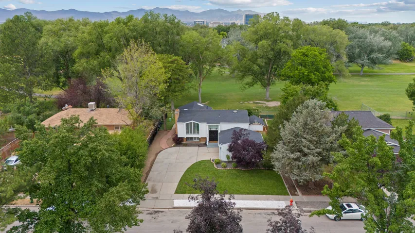 Manicured lawn, mature trees, paved driveway, curved sidewalk, and a surrounding green landscape