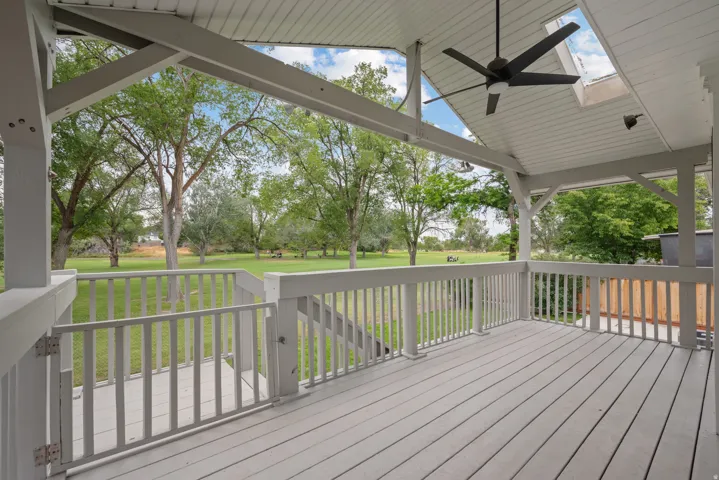 Covered outdoor deck with a ceiling fan, skylight, and white railing