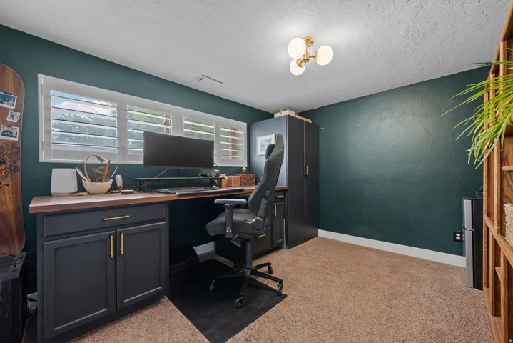 Custom built-in desk with wood-finish countertop, dark cabinetry with brass hardware, and white plantation shutters