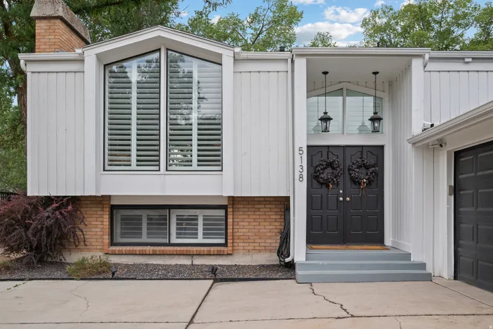 Double entry doors with transom window, two exterior pendant lights, board and batten siding, brick foundation, and an attached garage