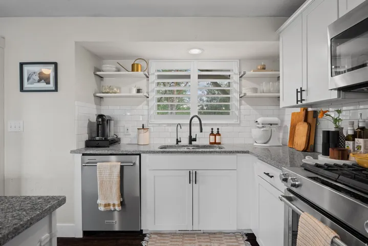 Modern kitchen featuring white cabinetry with brushed metal hardware, stainless steel appliances including a gas range and built-in microwave, subway tile backsplash, gray quartz countertops, open shelving with glass fronts, and a black gooseneck faucet o