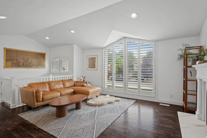 Vaulted white ceilings with recessed lighting, dark wood-finish flooring, white railing, and a multi-pane window with white plantation shutters
