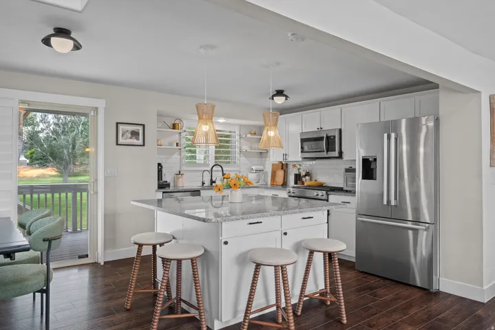 Kitchen featuring an island with stone countertop, stainless steel appliances, white cabinetry, and wood-finish flooring