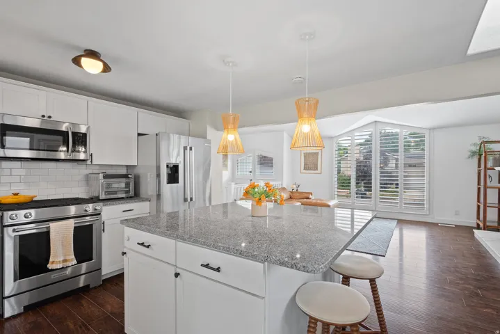 Kitchen featuring white cabinetry, stainless steel appliances, a large island with a stone-finish countertop, and wood-finish flooring