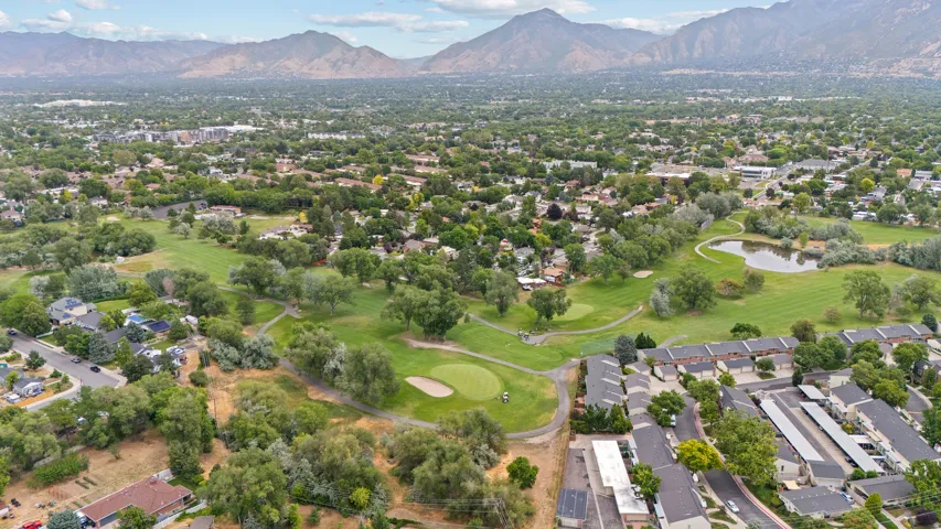 Aerial perspective showcasing a residential area, a golf course with greens and sand traps, and a pond feature