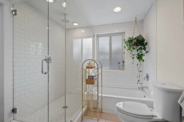 Glass-enclosed shower with white subway tile, a built-in tub, and a window with frosted panes