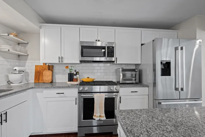Kitchen featuring white shaker-style cabinetry, stainless steel appliances, granite countertops, a white subway tile backsplash, and open shelving
