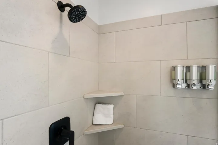 Shower featuring light-toned large format tile, matte black fixtures, and built-in corner shelving