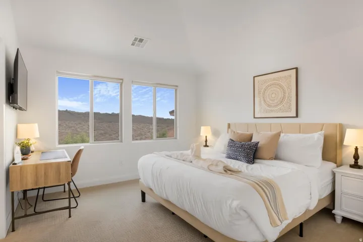 Carpeted room with white walls, two large windows, a sloped ceiling, and a built-in wall-mounted television