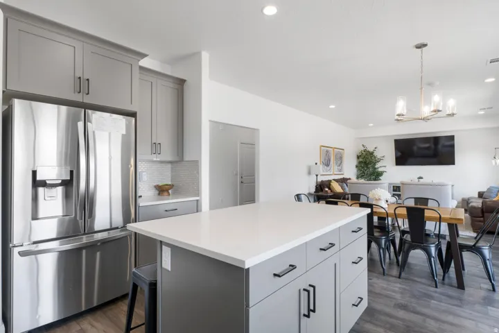 Kitchen island with light-colored countertop, stainless steel refrigerator, contemporary overhead lighting fixture, wood-finish flooring, and gray cabinetry with dark hardware