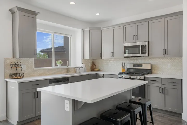 Contemporary kitchen featuring gray shaker-style cabinetry, white countertops, a mosaic tile backsplash, stainless steel appliances, and wood-finish flooring