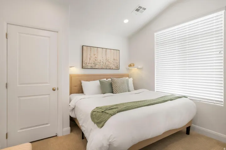 Vaulted ceiling with recessed lighting, large window with blinds, panel door, and wall-mounted sconces