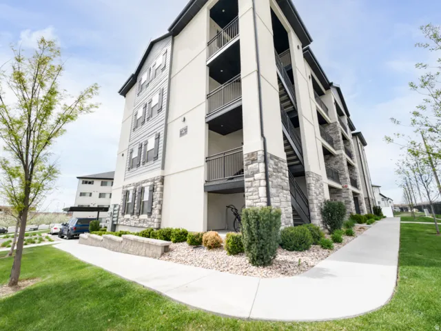Multi-story building with stone-clad lower levels, stucco siding, horizontal paneling, and private balconies with metal railings